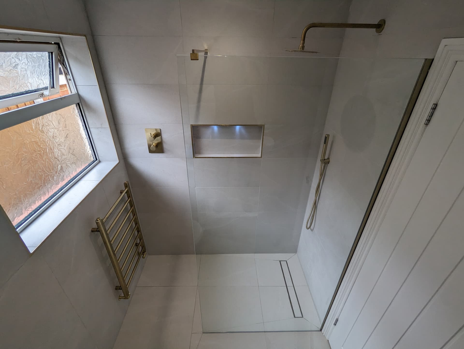 Walk-in wet room with brushed brass rainfall shower, recessed lit niche and linear drain