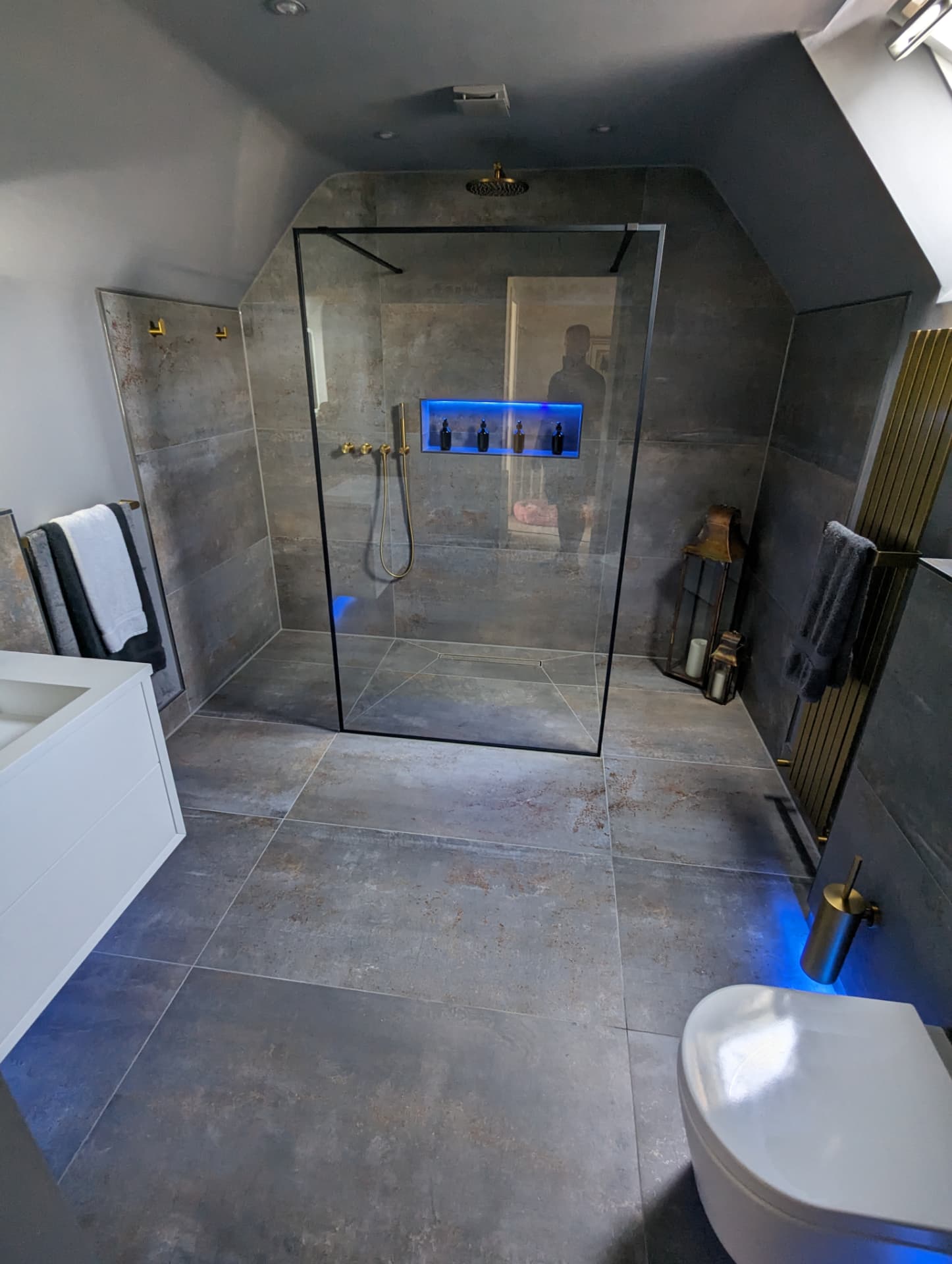 Loft bathroom with metallic stone tiling, black-framed walk-in shower screen and brushed brass fittings